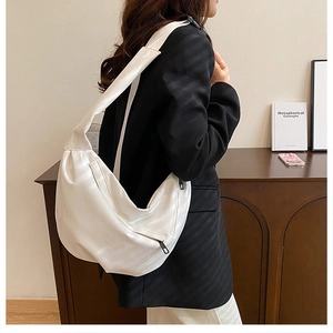 Detail showing the side view of a white crescent shoulder bag on a model in a black suit