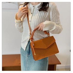 Detail of caramel brown croc-embossed handbag with knot handle and adjustable strap