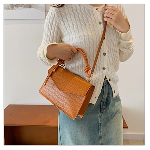 Detail of a brown crocodile texture leather crossbody bag styled with a white outfit