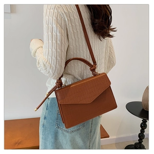 Detailed view of brown crocodile texture shoulder bag with stylish knot handle on model