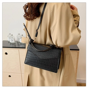 Detail of black crocodile texture leather crossbody bag with gold hardware and flap