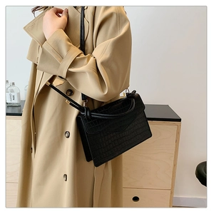 Detail of black faux crocodile leather crossbody bag with knot design on shoulder strap