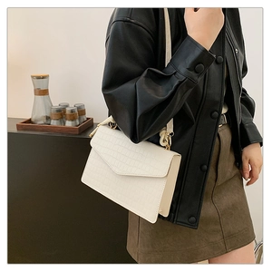 Detail of white crocodile pattern shoulder bag with gold hardware worn by a model