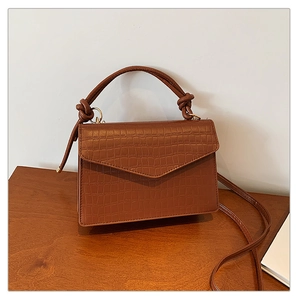 Detail of dark brown faux leather crossbody bag with elegant crocodile texture and gold hardware