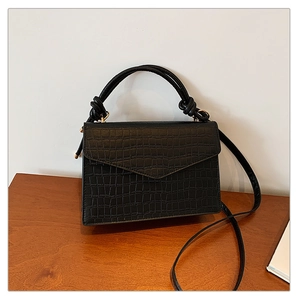 Detail of black faux leather handbag with crocodile pattern and knotted handle