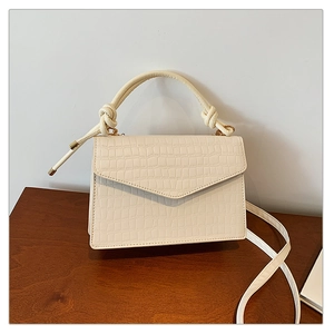 Detail of off-white crocodile texture crossbody bag with knotted handle and flap closure
