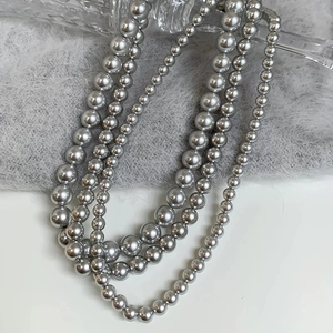 Detail of dark grey pearl necklaces in three sizes draped over a glass bottle