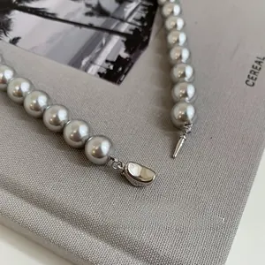 Macro detail of silver ingot clasp on pearl necklace over grey textured background
