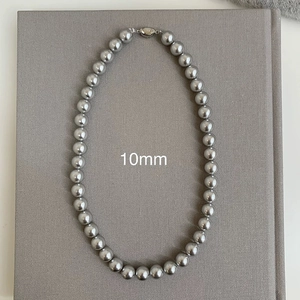 Macro detail of 10mm silver grey pearl necklace with metallic clasp on a textured book cover