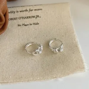 Minimalist silver knot hoop earrings on beige linen cloth with a polished mirror finish