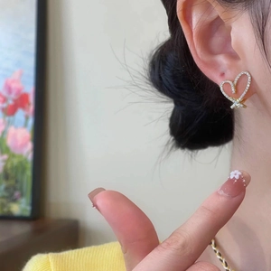 Close-up of heart-shaped gold earrings with paved cubic zirconia worn by model
