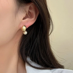 Elegant gold teardrop earrings with a white round pearl drop worn by a model