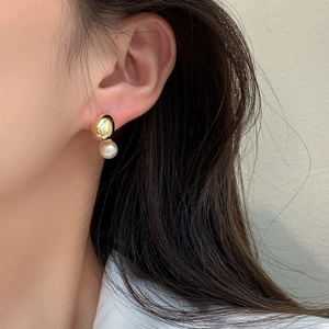 Detailed view of elegant gold metal stud earrings with dangling white pearls on a model