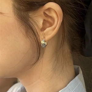 Silver twisted rope hoop earrings with layered metal texture worn by a model on the ear