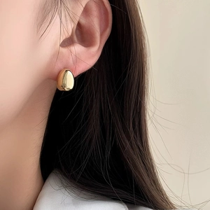 Close-up of minimalist golden teardrop stud earring with a polished mirror finish on ear