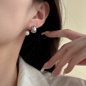 Close-up of liquid silver metal and white pearl stud earrings on a model's ear