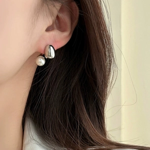Close-up of minimalist silver water drop stud earrings with round white pearls on a model