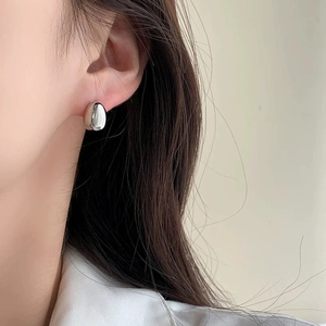 Detail shot of silver bean-shaped earrings with polished finish on model's ear