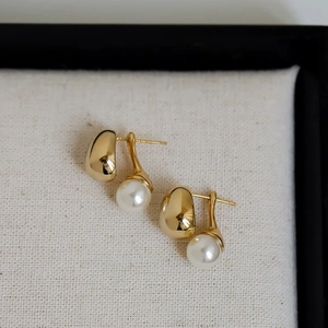 Detailed view of elegant gold bean studs with white round pearl drops on a textured fabric