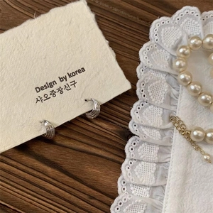 Detail view of silver hoop earrings with textured wave pattern on a display card