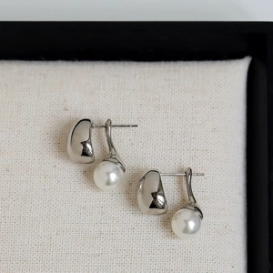 Detailed view of silver minimalist stud earrings with high-luster white pearls on fabric