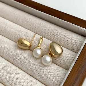 Macro detail of polished gold bean stud and glossy pearl components on white velvet padding