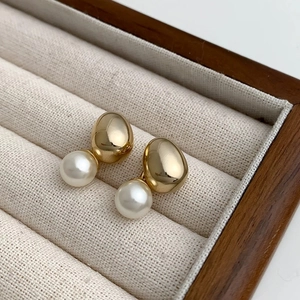 Close-up of elegant gold bean and white pearl stud earrings on a velvet tray