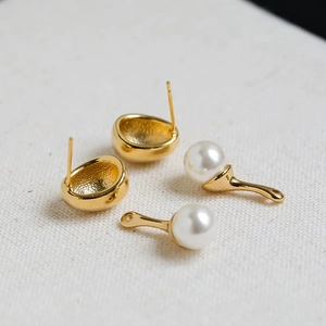 Macro detail of gold-plated stud earrings featuring detachable white pearls on textured fabric