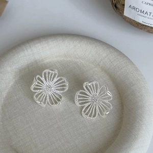 Macro view of silver hollow flower earrings with crystals on a textured stone plate