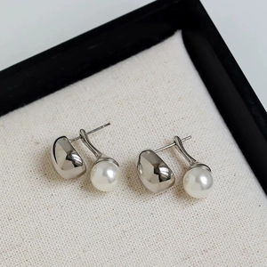 Detailed view of silver minimalist bean stud earrings with lustrous round pearls on linen