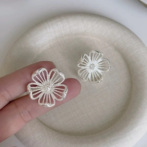 Detailed view of silver hollow flower stud earrings held on a fingertip for scale