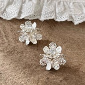 Detail of silver flower earrings with hammered petals and center zircon on leather background