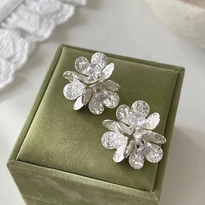 Close-up of zircon flower earrings with hammered petals on green velvet box
