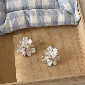 Detail of silver flower earrings with zircon centers on a textured wooden tray