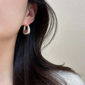 Close-up of a woman wearing thick silver-toned U-shaped hoop earrings with a polished finish