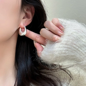 Close-up of polished silver teardrop hoop earrings worn by a model in a cozy white sweater