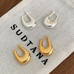 Close-up of gold and silver U-shaped polished hoop earrings on a linen bag