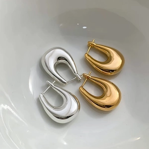 Close-up of minimalist U-shaped gold and silver earrings with a high-polished mirror finish