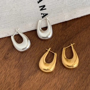Close-up of gold and silver U-shaped metal hoop earrings on textured linen background