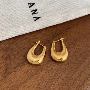 Polished gold U-shaped earrings on a dark walnut table with a premium linen pouch