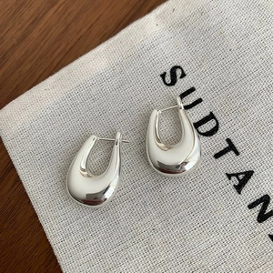 Polished silver U-shaped chunky hoop earrings displayed on a rustic canvas and wood background
