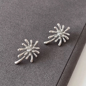 Detailed view of silver firework stud earrings with a radial design on a textured gray base
