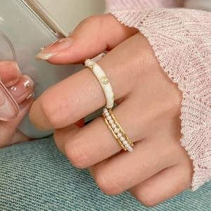 Detail of elegant gold-plated rings with cream enamel, zircon, and layered pearls