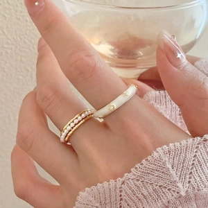 Close-up of elegant gold pearl ring and cream enamel floral ring set on model hand