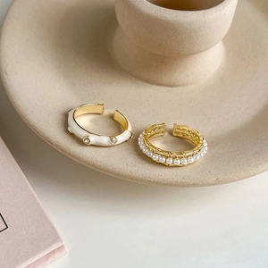 Elegant gold rings featuring white enamel drip oil and faux pearls on a ceramic stand