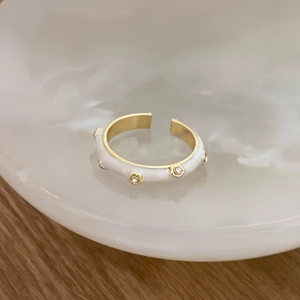 Detailed close-up of white enamel gold ring with tiny zircons on a ceramic tray