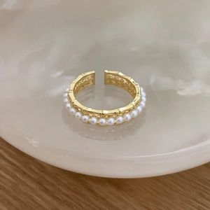 Detailed view of bamboo-textured gold ring with white pearl inlay on a decorative tray