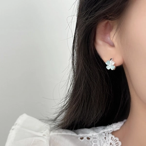 Elegant silver four-leaf flower earrings with blue zircon on female model's ear