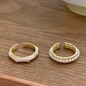Detail of minimalist gold open rings with white enamel and delicate pearls on wood