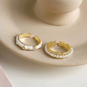 Macro detail of gold adjustable rings with white enamel and delicate micro pearls